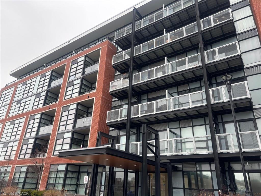 Modern multi-story building featuring brick and glass exterior, multiple balconies with glass railings, and a prominent entrance canopy