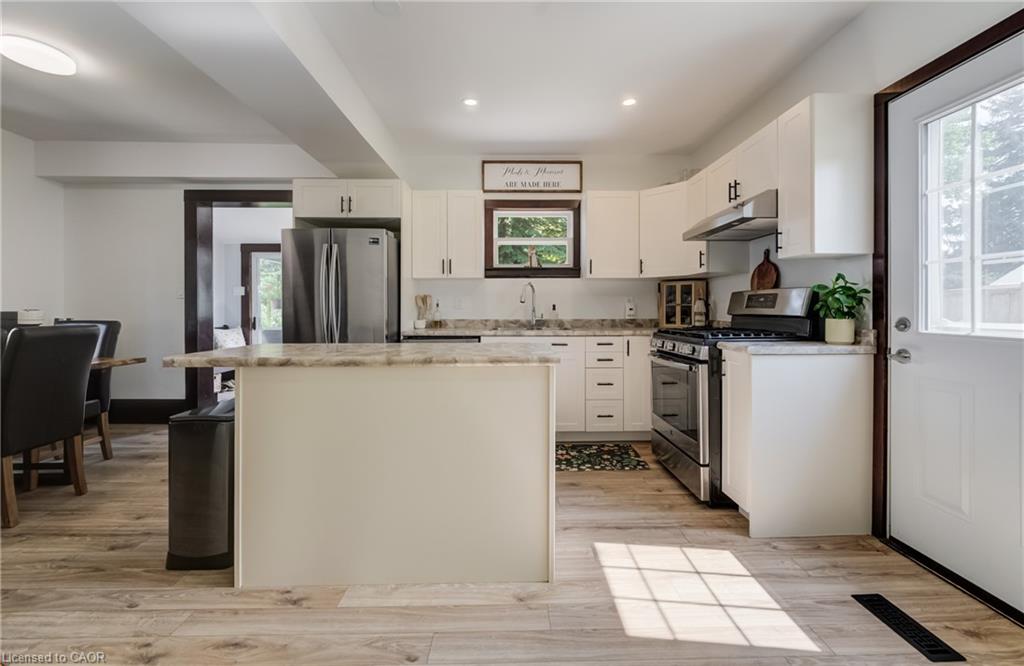 White cabinetry, stainless steel appliances, wood-finish flooring, recessed lighting, and a kitchen island with seating