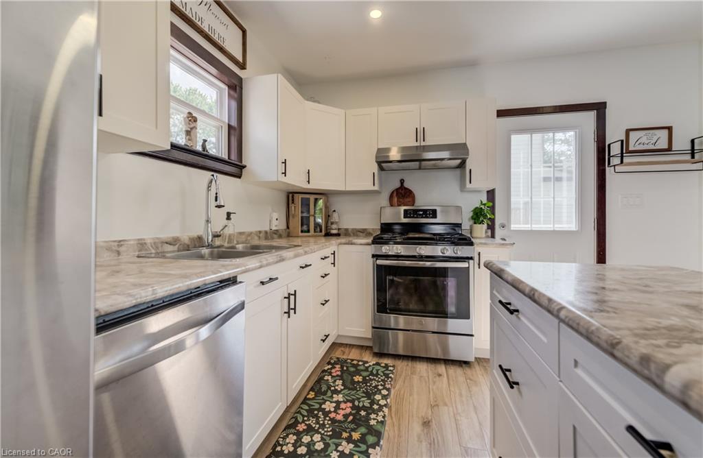White cabinetry with matte black hardware, stainless steel appliances, wood-finish flooring, and light-toned countertops