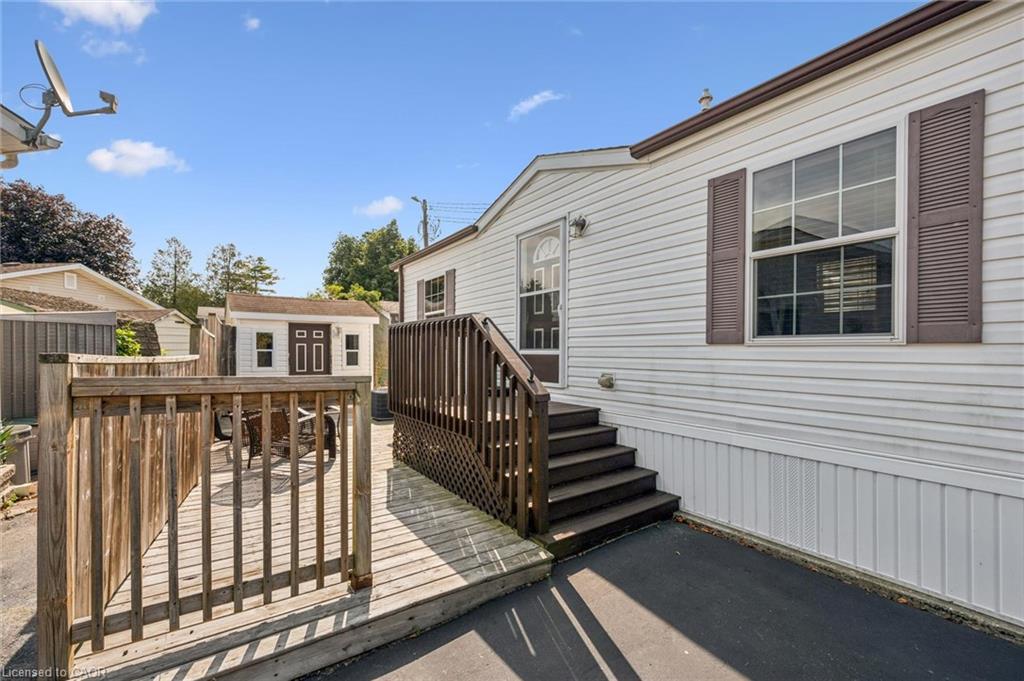 Wood deck and ramp with railings, exterior storage shed, white vinyl siding, brown louvered shutters, and dark steps