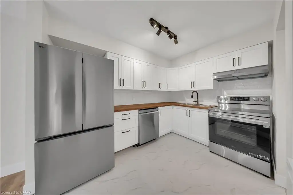 Modern kitchen featuring white shaker cabinetry, stainless steel appliances, butcher block countertops, and white subway tile backsplash