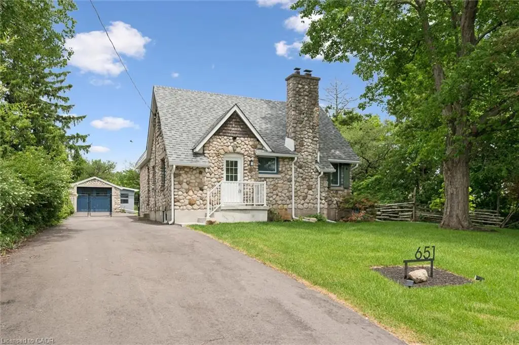 Stone exterior with a prominent stone chimney, gabled roof, paved driveway, and detached garage with blue doors