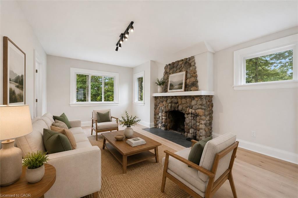 Stone fireplace with a white mantel, track lighting, light wood-finish flooring, and multiple windows
