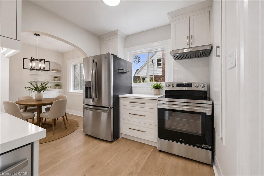 Modern kitchen featuring stainless steel appliances including a French-door refrigerator, electric range, and built-in microwave, paired with white cabinetry and wood-finish flooring
