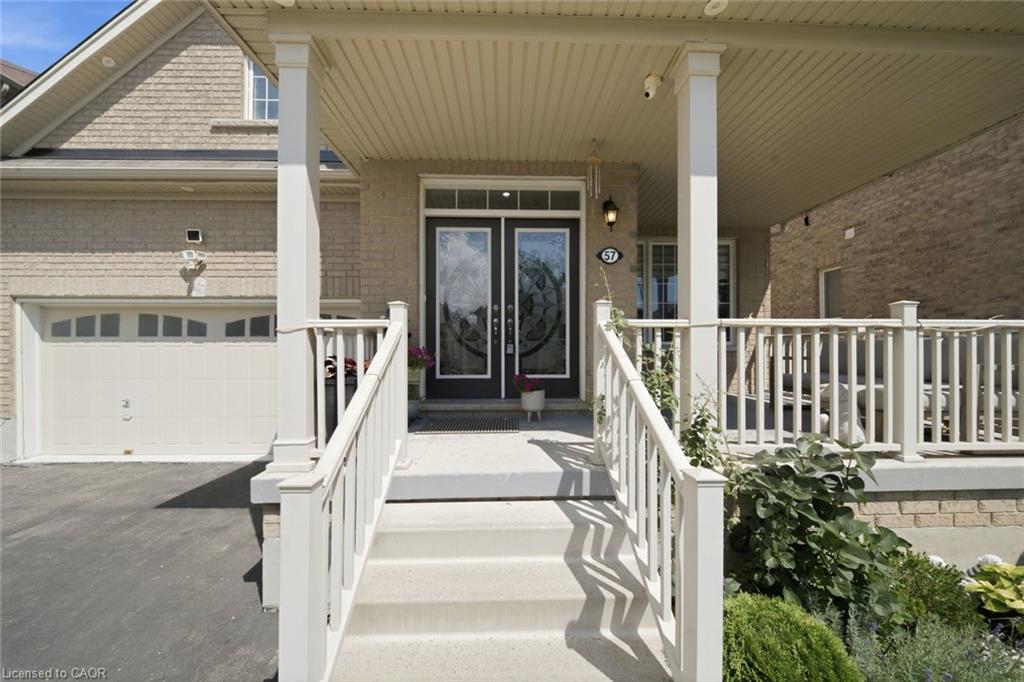 Covered porch with white railings and columns, featuring a double door entry with decorative glass, light brick exterior, and an attached garage