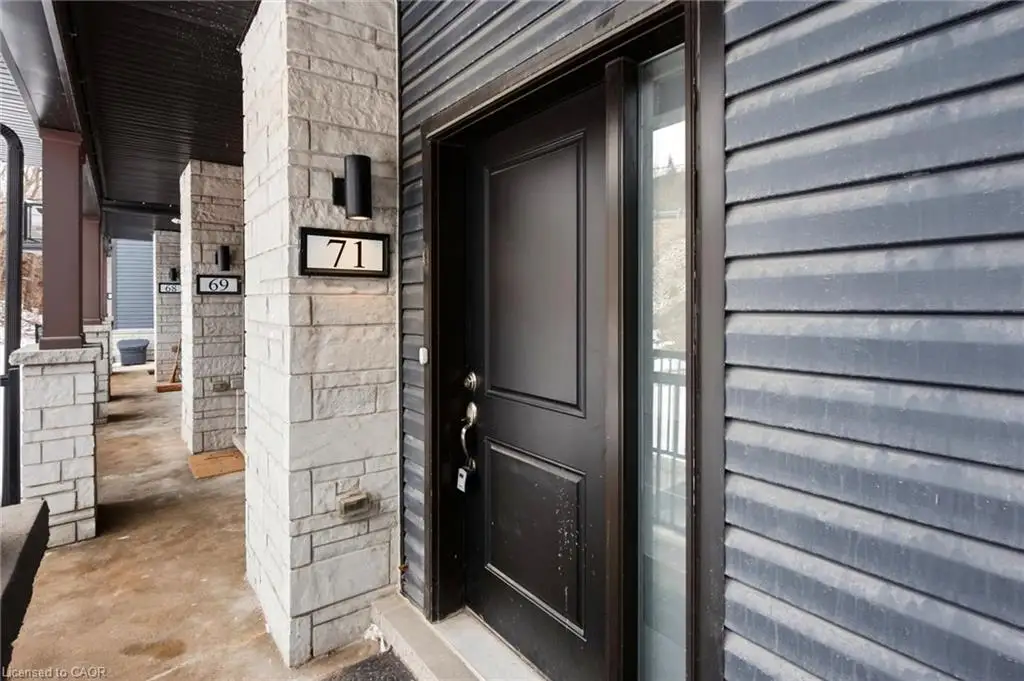 Exterior entrance featuring dark horizontal siding, stone veneer support pillars, a solid door with sidelight, and cylindrical wall-mounted exterior lighting