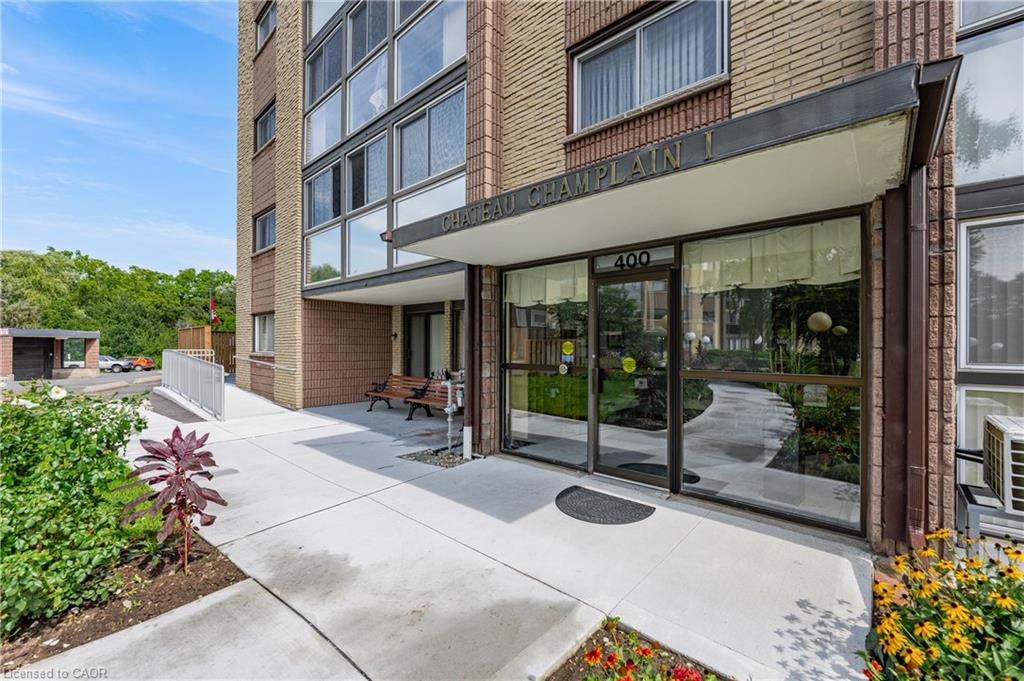 Building exterior featuring brick facade, concrete pathways, a covered entry, and lush landscaping