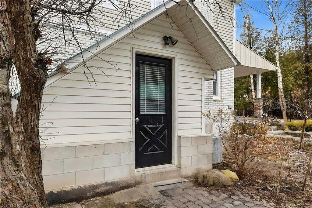 Exterior entry featuring a black door with integrated blinds, white horizontal siding, and concrete block foundation