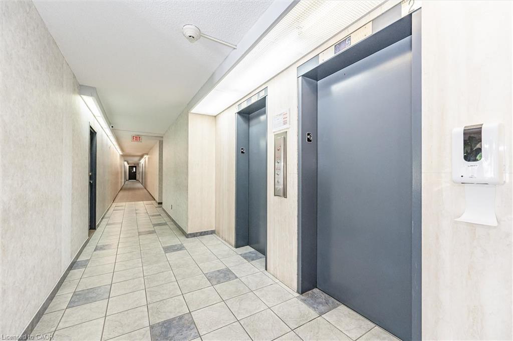 Hallway with two elevator doors, tiled flooring, textured wall finishes, and overhead lighting