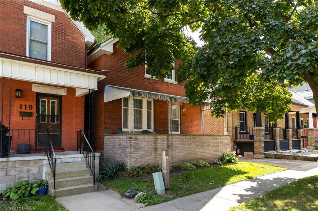 Brick exterior with a covered front porch featuring wrought iron railings, mature trees, and a front yard with established landscaping