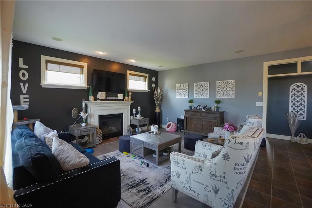 Living area featuring a white mantel fireplace, recessed lighting, two windows with blinds, wood-finish flooring, and a decorative doorway with an arched transom
