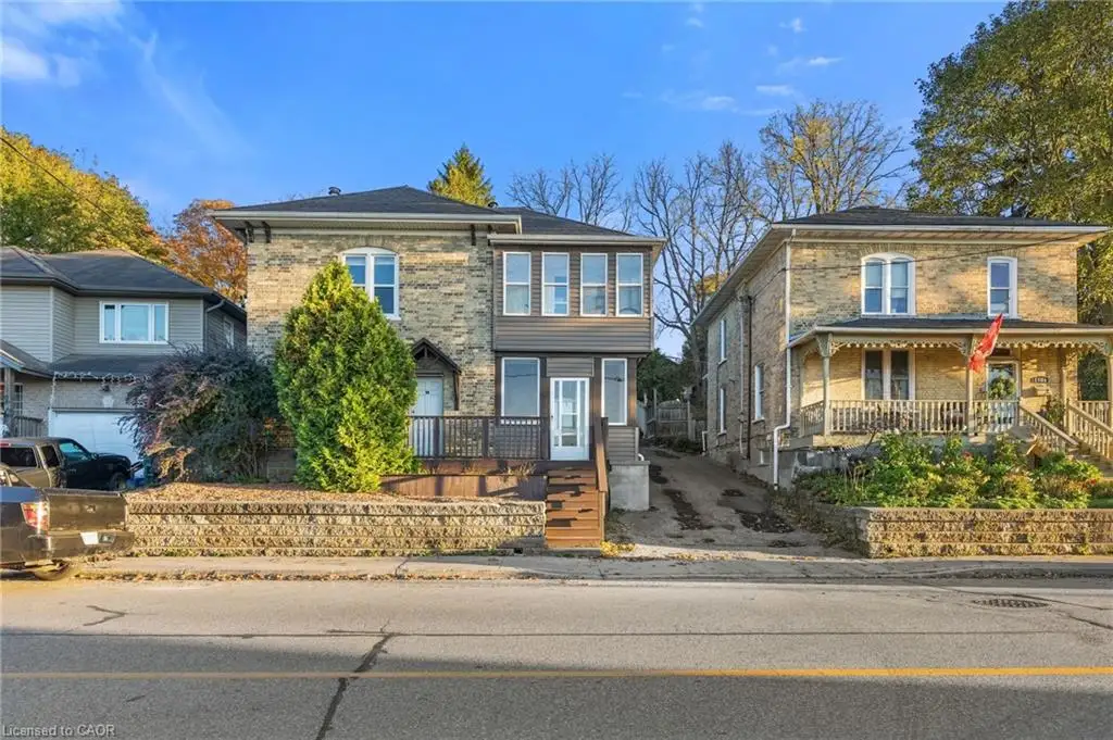 Two-story masonry exterior featuring stone facade, multi-pane windows, wood-finish deck with railing, and stone retaining wall