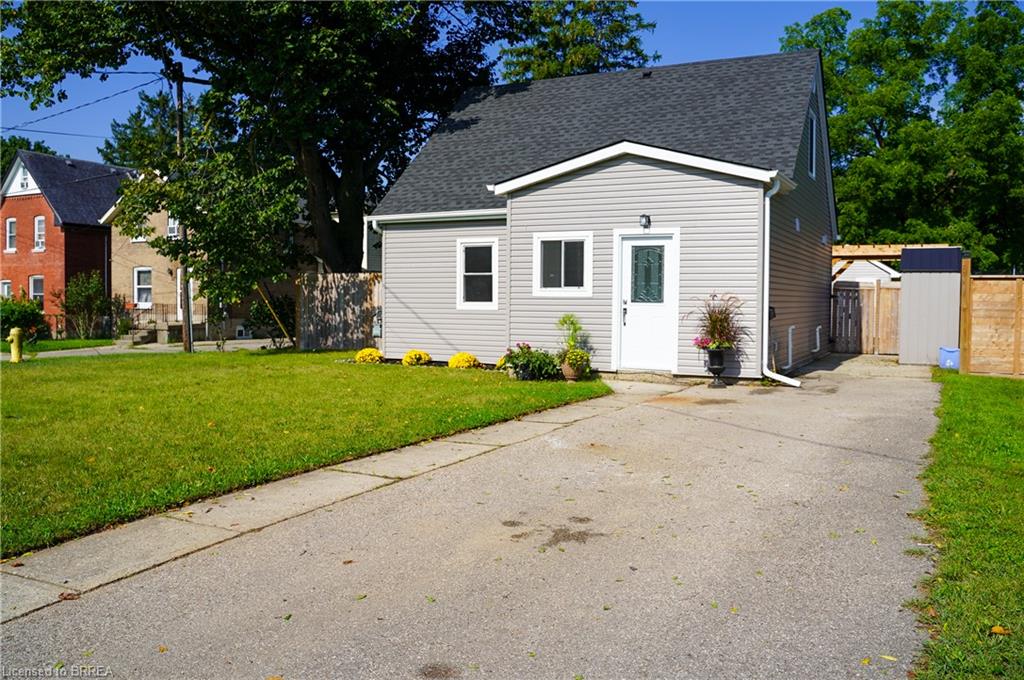 Light gray siding exterior with a dark shingle roof, featuring a white entry door and a paved driveway