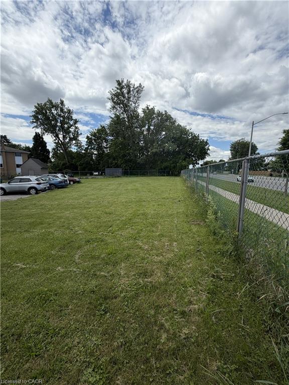 Expansive grass lot featuring a chain-link fence border and mature trees
