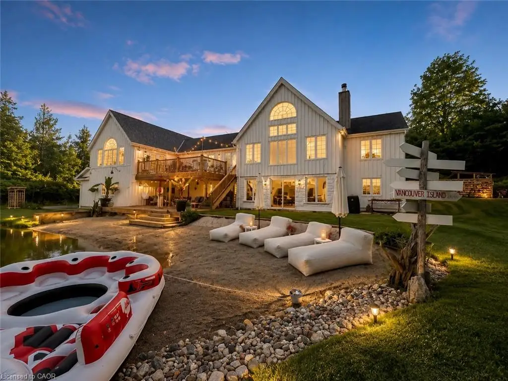 White vertical siding exterior with a multi-level wood deck, ground-level patio, and a sandy beach area