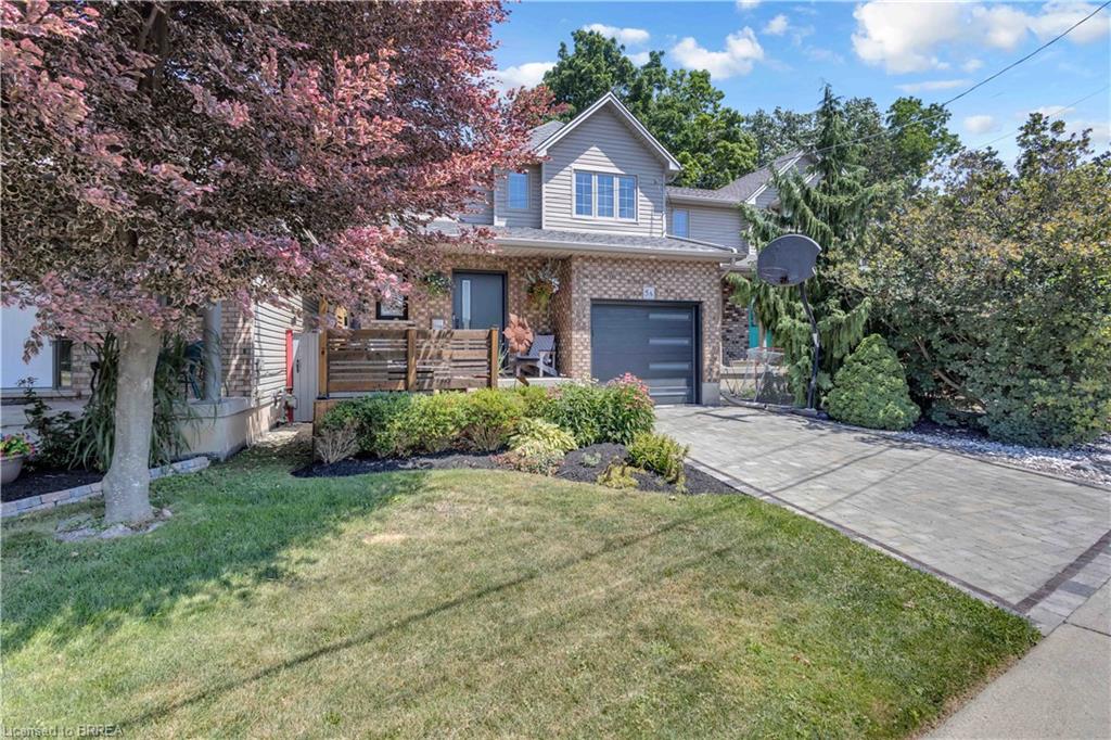 Brick and siding exterior with an attached garage, paver driveway, and mature landscaping
