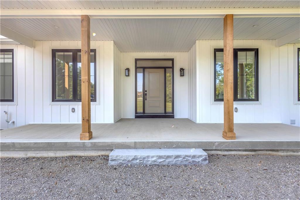 Covered front porch with wood columns, white board and batten siding, black-framed windows, and a black-framed front door with sidelights