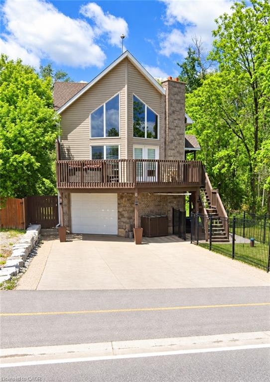Gable roofline with large picture windows, stone veneer accents, and a spacious elevated wood deck with railing
