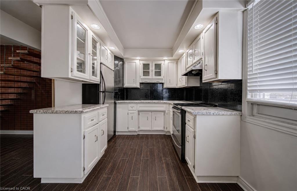 Modern kitchen featuring white cabinetry, a dark tile backsplash, stainless steel appliances, and wood-finish flooring