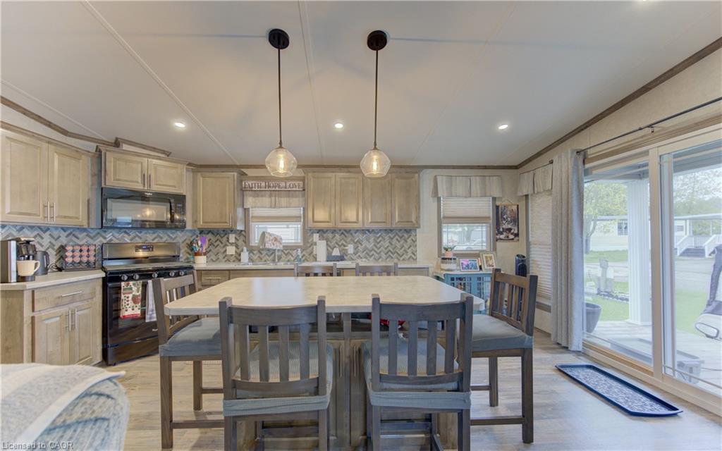 Open-concept kitchen featuring an eat-at island with seating for four, light wood-finish cabinetry, a herringbone pattern tile backsplash, stainless steel appliances, and two pendant light fixtures