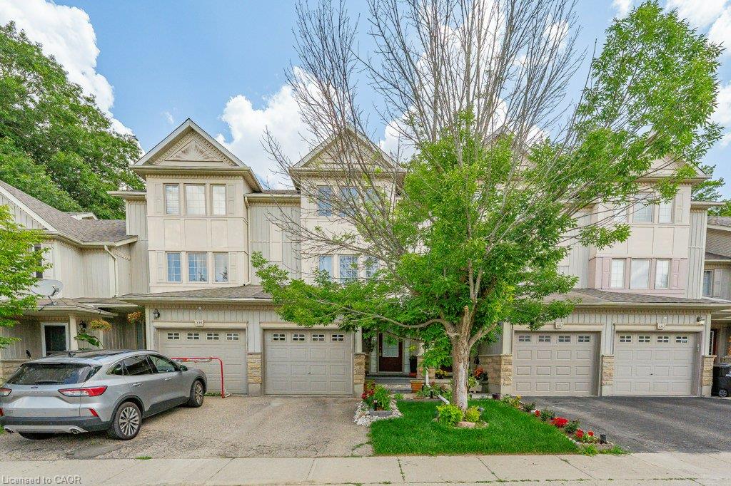 Multi-level townhome exterior featuring light-colored siding, multiple garage doors, and front entry landscaping