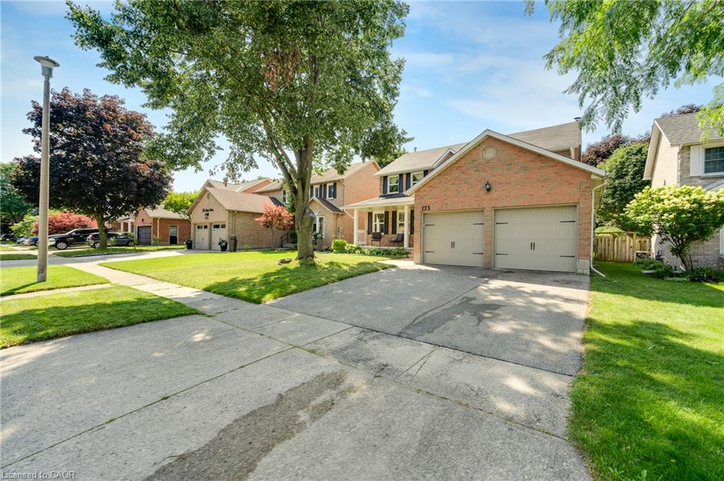 Brick exterior with a dual garage, concrete driveway, and a front lawn with mature trees