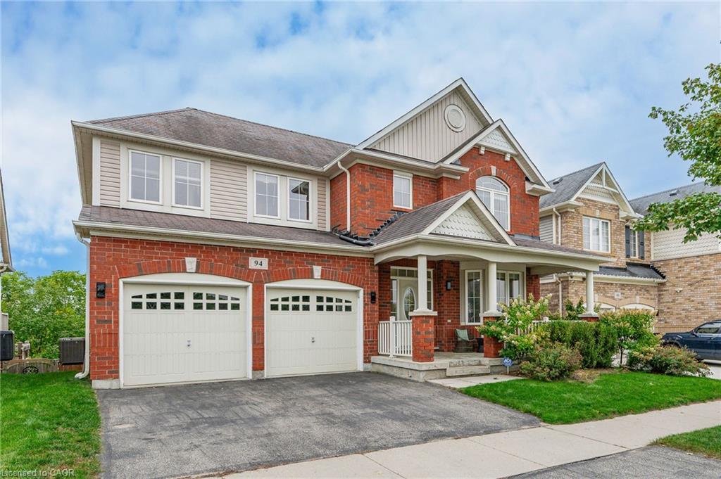 Elegant two-story brick colonial with dual-car garage, featuring a welcoming front porch with gabled roofline, white trim detailing, and professional asphalt driveway