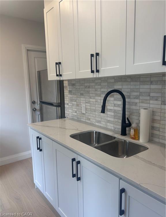 White shaker cabinetry with black hardware, double basin stainless steel sink, black gooseneck faucet, light-toned wood-finish flooring, and a patterned tile backsplash