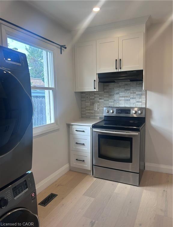 White shaker-style cabinetry with matte black hardware, stainless steel electric range, tile backsplash, light wood-finish flooring, and recessed ceiling lighting