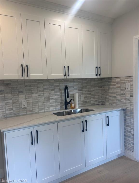 White shaker-style cabinetry with matte black hardware, dual-basin stainless steel sink with a matte black faucet, and a tiled backsplash