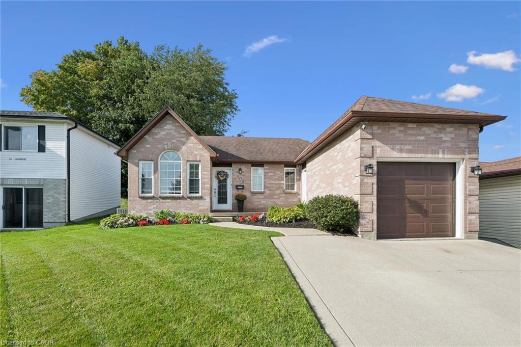 Brick exterior with an arched window, attached garage, concrete driveway, and cultivated landscaping