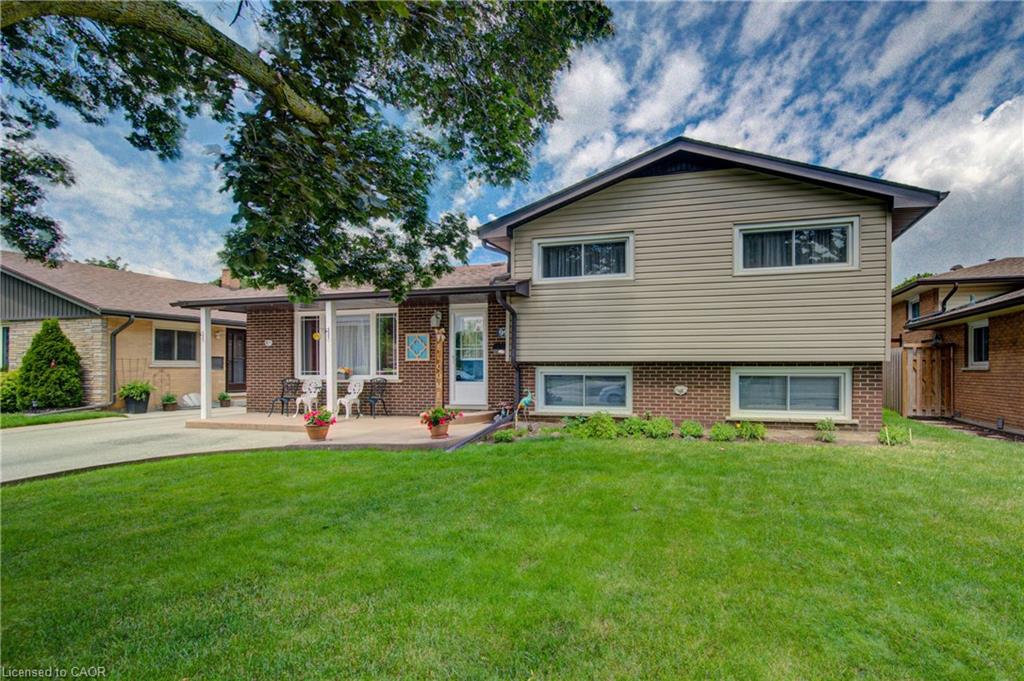 Residential exterior featuring a split-level design with brick and siding facade, a manicured front lawn, a paved driveway, and a covered front patio