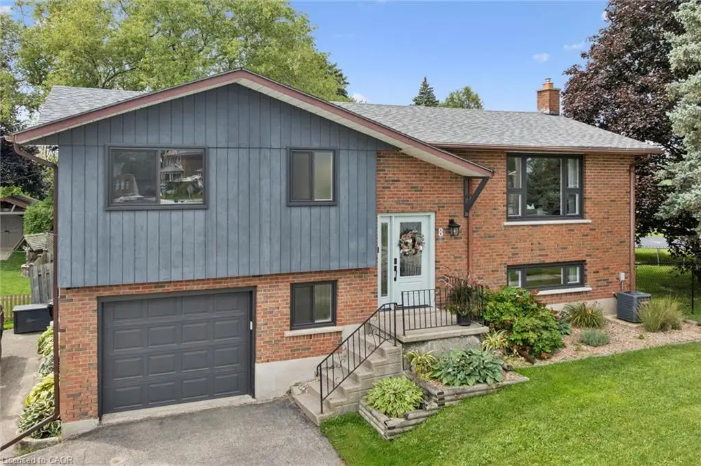 Split-level residence featuring brick and vertical siding, a paved driveway, an attached garage, and mature landscaping