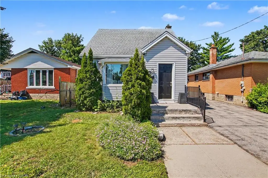 Gable roofline, light-colored siding, front entry steps with railing, established front landscaping, and a paved driveway