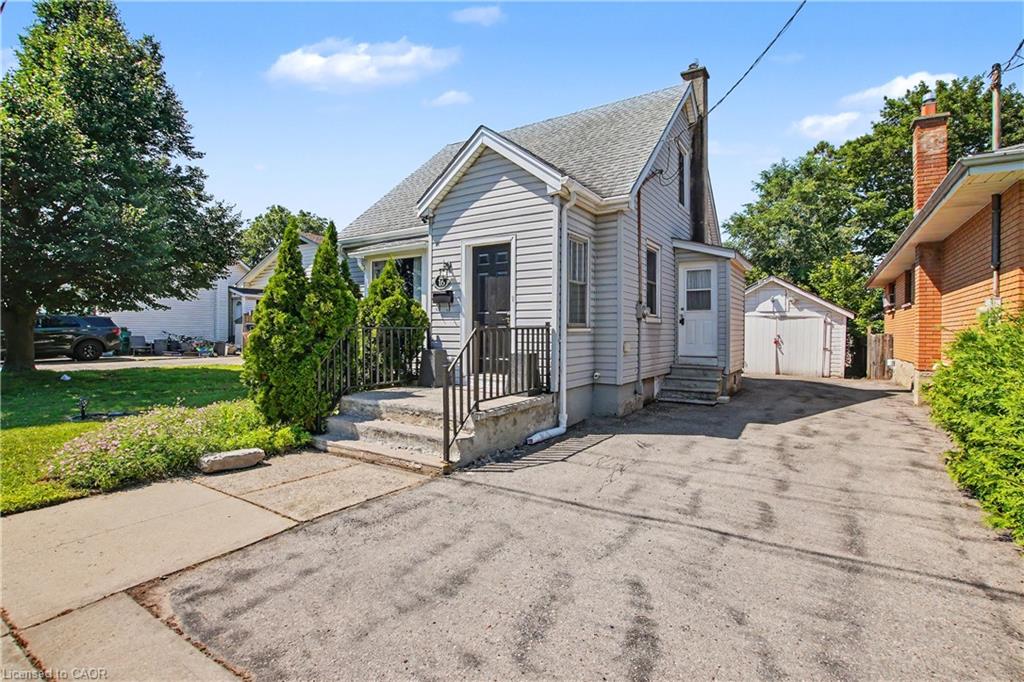 Gabled roofline, siding exterior, paved driveway, detached garage, and mature trees