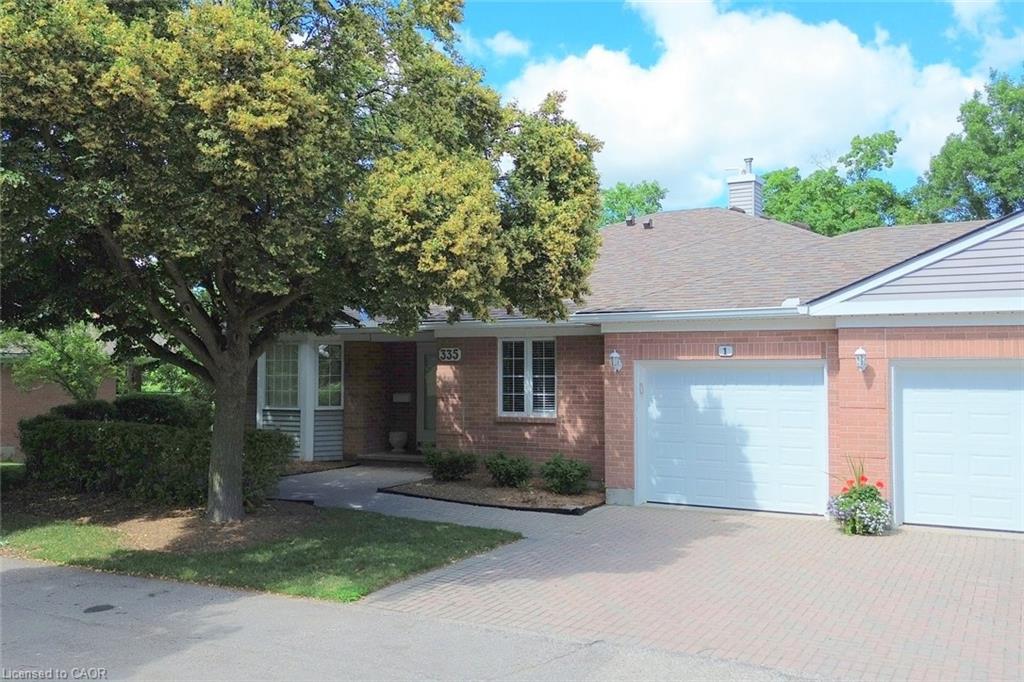 Brick exterior featuring a multi-car paved driveway, attached garages, and a prominent front tree