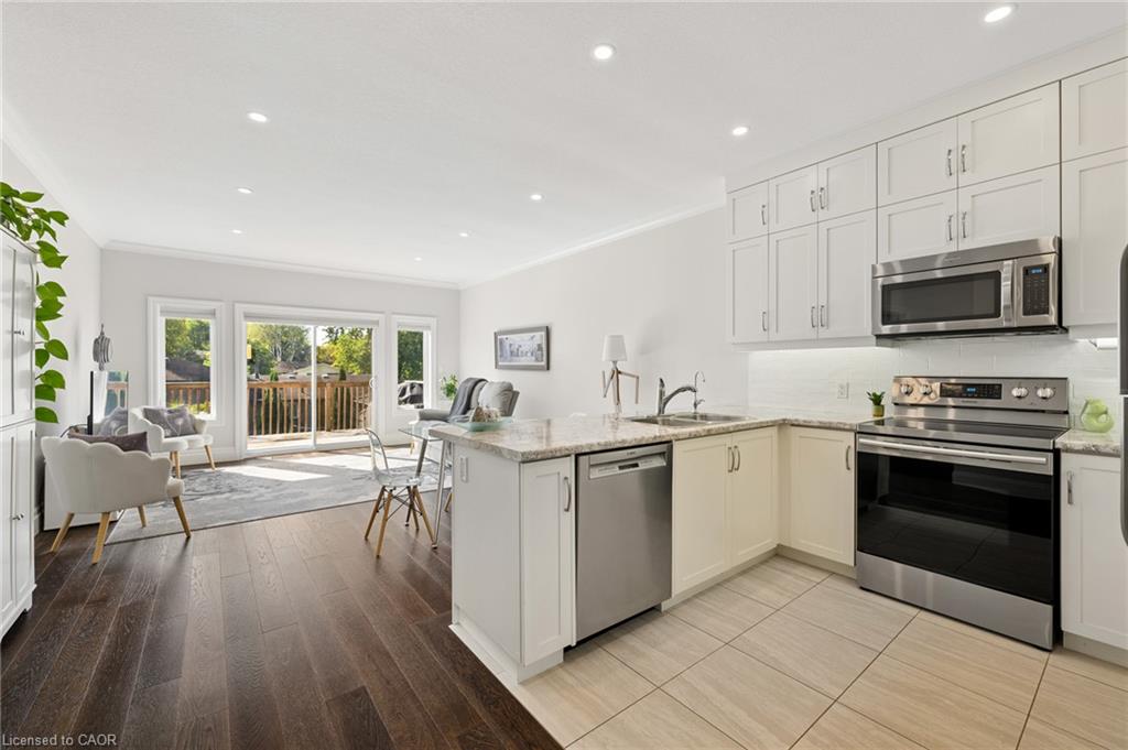 Open-concept living area with dark wood-finish flooring, white shaker cabinetry, stainless steel appliances, and a sliding glass door to an outdoor deck