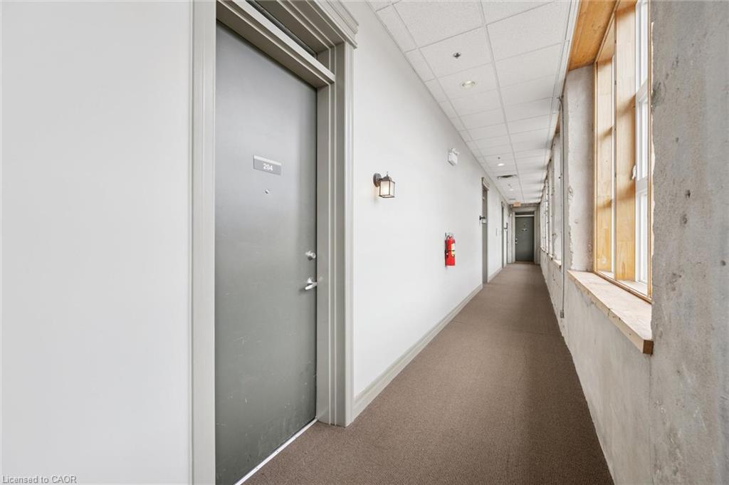 Hallway featuring textured carpet flooring, recessed lighting, wall-mounted light fixtures, and a series of windows with wooden framing