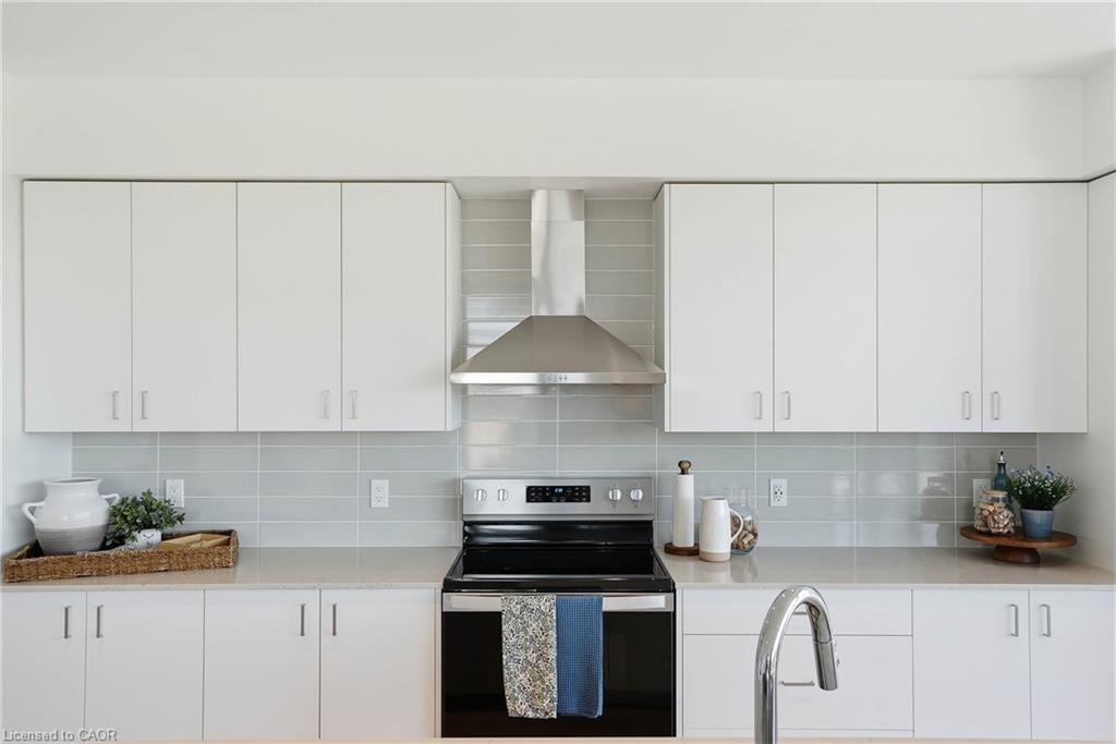 Modern kitchen featuring crisp white cabinetry with brushed nickel hardware, light gray subway tile backsplash, stainless steel appliances including a range hood, and a sleek pull-down faucet above the sink