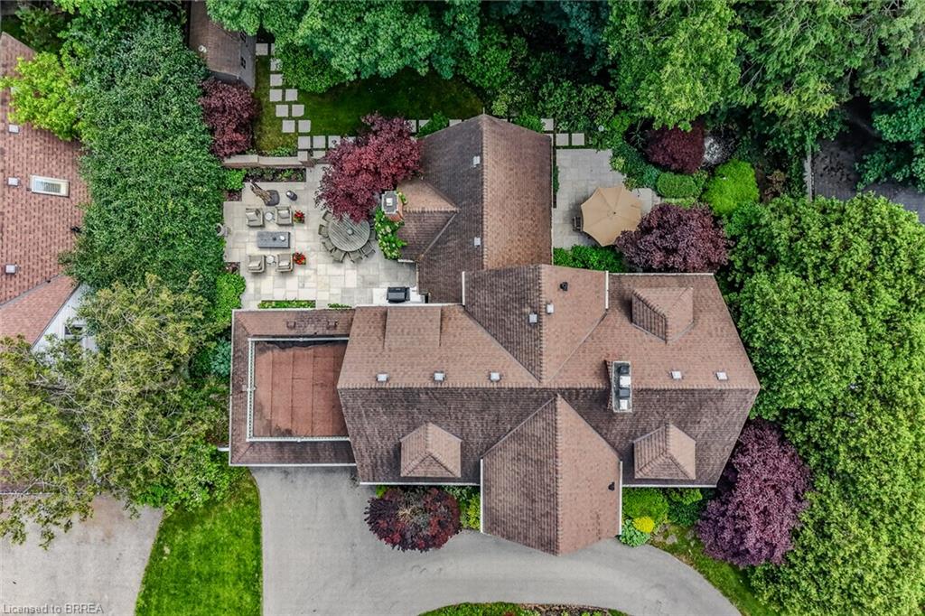 Expansive property featuring a multi-gabled roofline, paver patio, stone fire pit, lush landscaping, and a curvilinear driveway