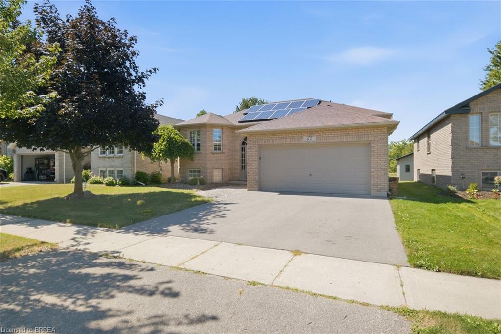 Brick exterior residence featuring a two-car garage, solar panels, and a paved driveway