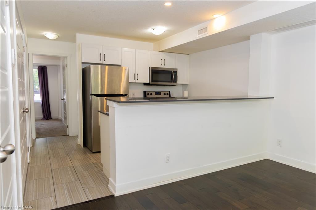 Kitchenette featuring white cabinetry, stainless steel appliances, dark countertops, and a breakfast bar