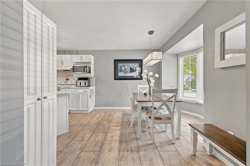 Kitchen and dining area featuring wood-finish flooring, white cabinetry, a bay window, a linear pendant light fixture, and a built-in pantry