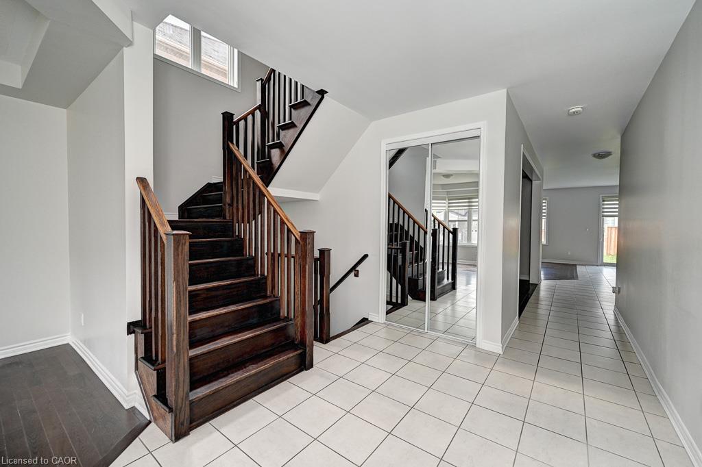 Wood-finish staircase with coordinating wood-finish handrails, white wall paint, square tile flooring, and mirrored sliding closet doors