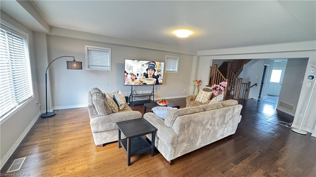 Wood-finish flooring throughout, multiple windows with blinds, and an open entryway to a wooden staircase with balusters