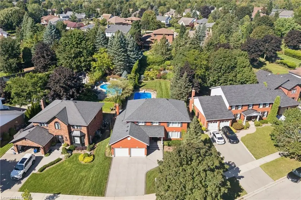 Brick exterior residence with a double garage, mature trees, manicured lawns, and a private swimming pool