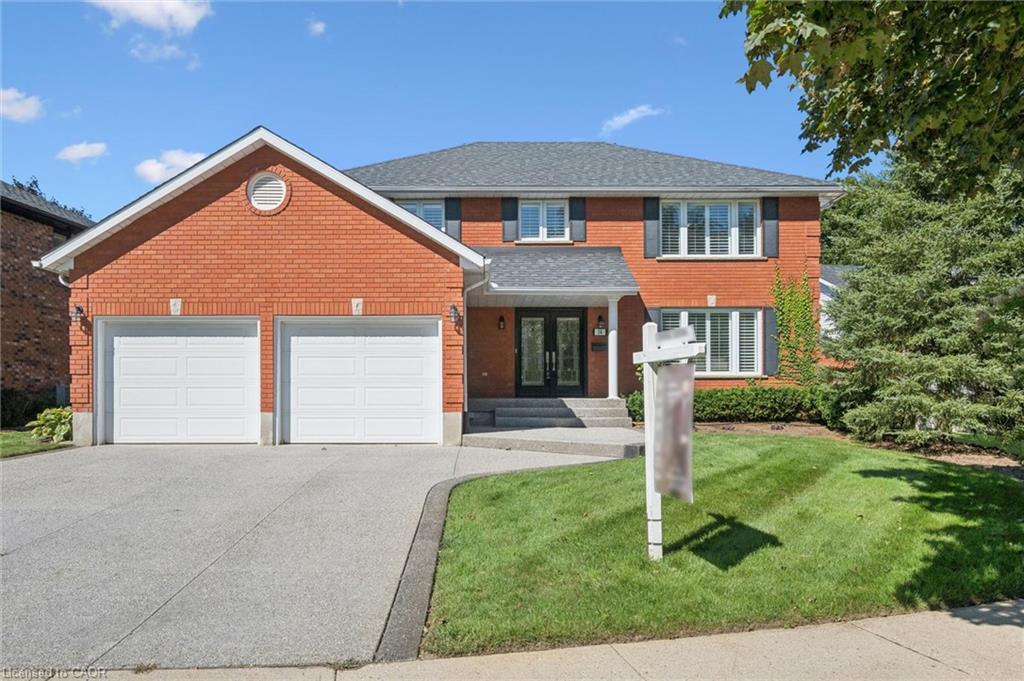 Red brick exterior with white trim, two-car garage, mature landscaping, and an asphalt shingle roof