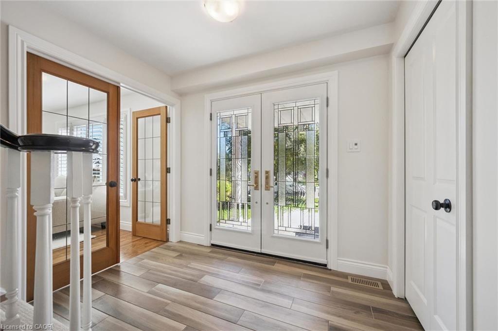 Double entry doors with decorative glass panels, wood-finish flooring, two paneled doors with grid glass inserts, painted white trim, and a white baluster railing