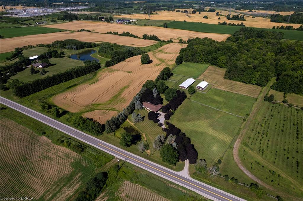 Expansive rural property featuring a main residence, cultivated fields, wooded areas, two white outbuildings, and a pond