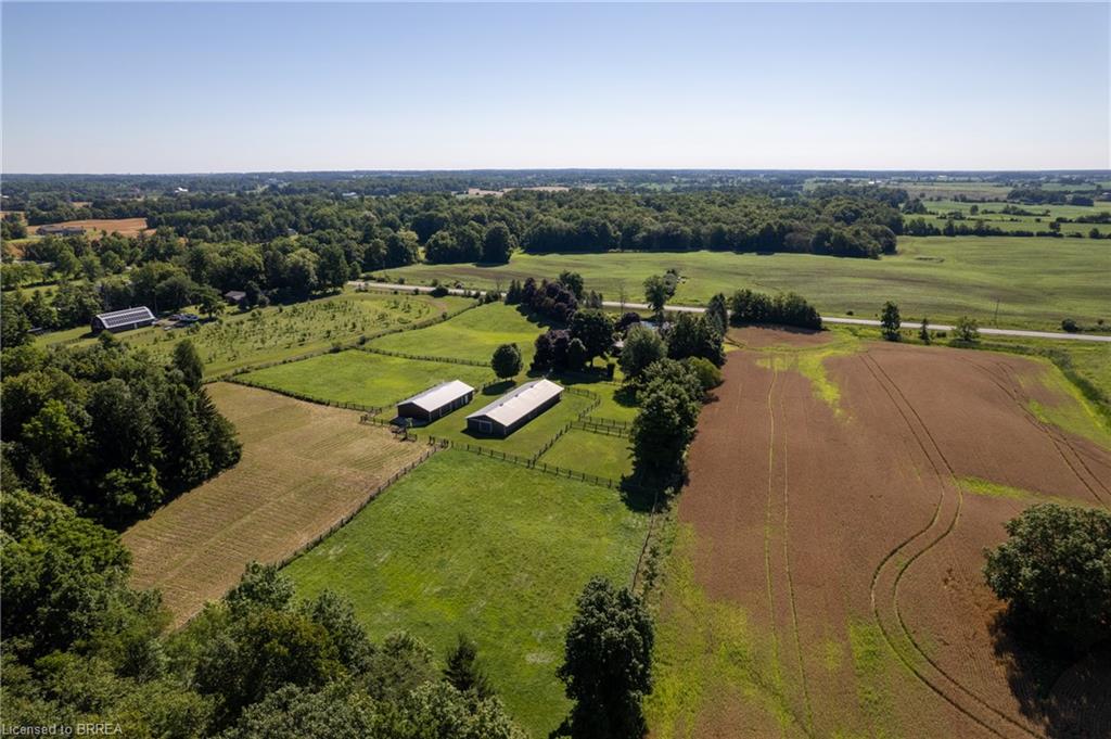 Expansive agricultural property featuring multiple fenced pastures, two large outbuildings with light-colored roofs, and cultivated fields